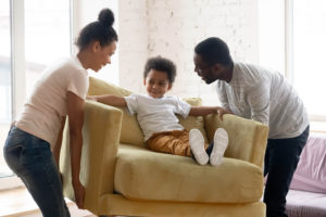 Couple rearranging furniture while son sits in chair